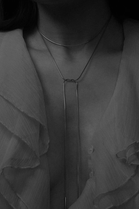 A handcrafted choker combining two 33 mm silver tube elements with a 120 cm chain. Designed for versatile styling, the chain can be tied, layered, or worn loose, including as a back neckline accent. Elegant silver ends ensure a perfect drape and refined finish. Discover modern, adaptable jewelry by UMIAR jewelry.