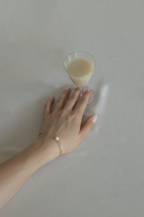 A minimalist bracelet made from a slim rigid half-hoop, finished with a natural pearl. Its smooth, flowing form highlights the wrist with subtle elegance, offering a timeless and classic look. Inspired by the GRANO BACCA earrings, it blends refined simplicity with signature design. Discover understated sophistication by UMIAR jewelry.