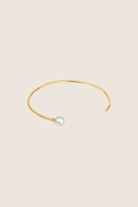 A minimalist bracelet made from a slim rigid half-hoop, finished with a natural pearl. Its smooth, flowing form highlights the wrist with subtle elegance, offering a timeless and classic look. Inspired by the GRANO BACCA earrings, it blends refined simplicity with signature design. Discover understated sophistication by UMIAR jewelry.