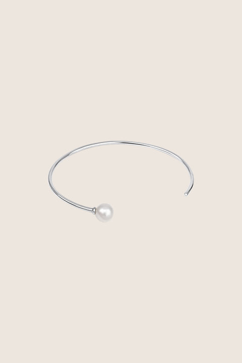 A minimalist bracelet made from a slim rigid half-hoop, finished with a natural pearl. Its smooth, flowing form highlights the wrist with subtle elegance, offering a timeless and classic look. Inspired by the GRANO BACCA earrings, it blends refined simplicity with signature design. Discover understated sophistication by UMIAR jewelry.