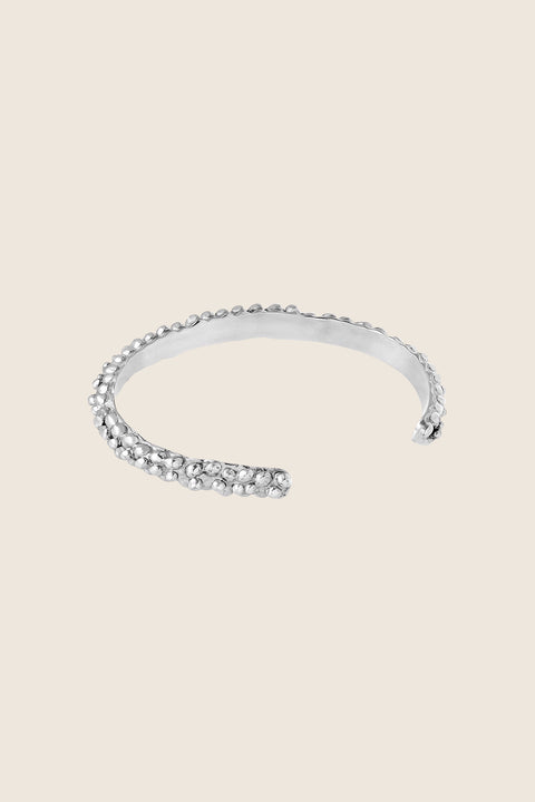 A rigid silver bangle with a distinctive granulated, speckled texture that beautifully reflects light and adds depth. Elegant worn alone or styled with the PELLO bracelet, it offers timeless sophistication and expressive design. A refined statement for lovers of unique, enduring jewelry. Discover sculptural elegance by UMIAR jewelry.