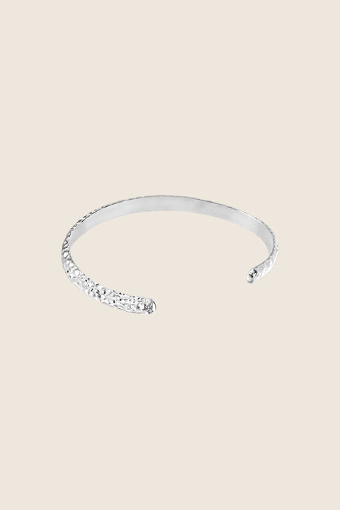 A rigid silver bangle inspired by hammered textures, designed to reflect light and emphasize a sculptural, three-dimensional form. Elegant worn solo or styled with the CRATER bracelet, it offers refined strength and timeless appeal. Discover expressive craftsmanship and modern elegance by UMIAR jewelry.