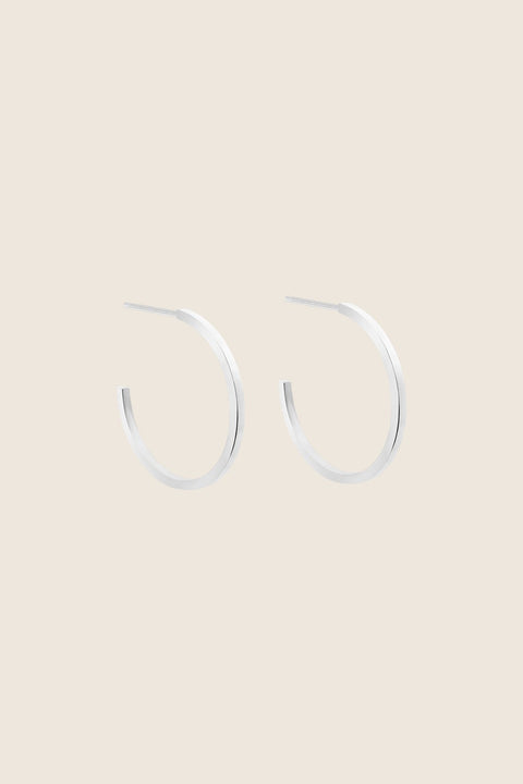 Delicate square-profile hoop earrings with a modern geometric character. Featuring a 23 mm diameter, they bring a contemporary edge to a classic form and can be worn alone or layered with ACTA MICRO. A timeless everyday essential. Discover refined minimalism by UMIAR jewelry.