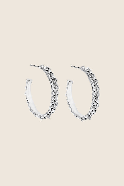 Large hoop earrings inspired by the sculptural surface of the moon, featuring a speckled, textured silver finish. With a 30 mm diameter, their irregular granulated structure reflects light beautifully, creating a bold yet elegant statement for evening wear. Discover expressive design by UMIAR jewelry.
