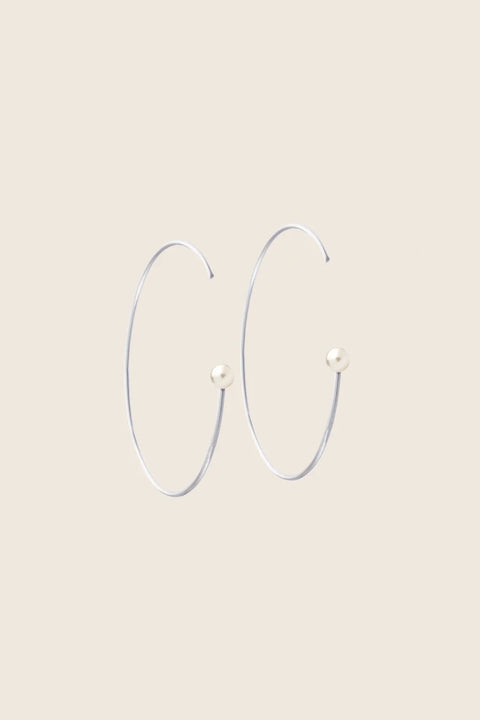 Large minimalist hoop earrings made from fine wire and accented with a natural pearl. Featuring a 45 mm diameter and a thread-through design with no clasp, they offer a refined yet expressive look. A modern statement piece perfect for special occasions. Discover contemporary elegance by UMIAR jewelry.