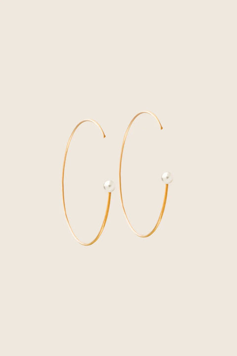 Large minimalist hoop earrings made from fine wire and accented with a natural pearl. Featuring a 45 mm diameter and a thread-through design with no clasp, they offer a refined yet expressive look. A modern statement piece perfect for special occasions. Discover contemporary elegance by UMIAR jewelry.