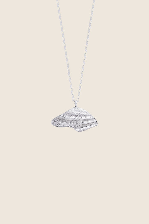 A delicate pendant inspired by the form of a broken shell, measuring 10 x 20 mm and suspended on a 40 cm chain. Combining organic texture with minimalist abstraction, this necklace captures timeless marine elegance. Ideal for summer looks and layering with the MARE II pendant. Discover refined seaside design by UMIAR jewelry.
