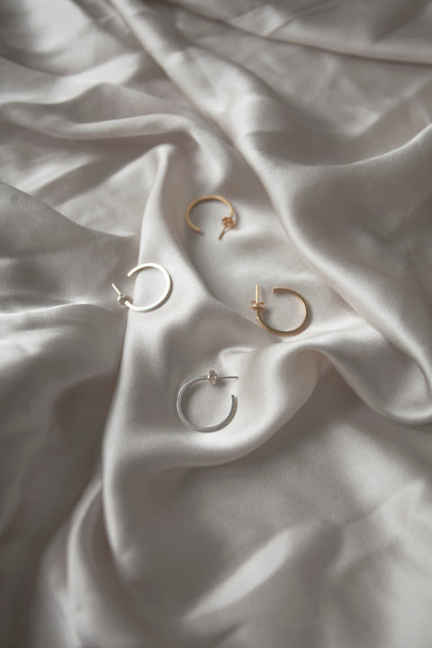 Delicate square-profile hoop earrings with a modern geometric character. Featuring a 23 mm diameter, they bring a contemporary edge to a classic form and can be worn alone or layered with ACTA MICRO. A timeless everyday essential. Discover refined minimalism by UMIAR jewelry.