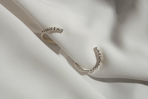 Large hoop earrings inspired by the sculptural surface of the moon, featuring a speckled, textured silver finish. With a 30 mm diameter, their irregular granulated structure reflects light beautifully, creating a bold yet elegant statement for evening wear. Discover expressive design by UMIAR jewelry.
