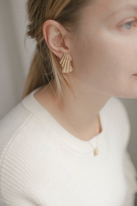 Elegant ear clips inspired by broken shells, designed as a summer statement in a refined form. Measuring 15 x 29 mm, they offer a stylish alternative to pierced earrings and add character to warm-weather looks. A sculptural accent that blends ease with elegance. Discover summer-ready design by UMIAR jewelry.