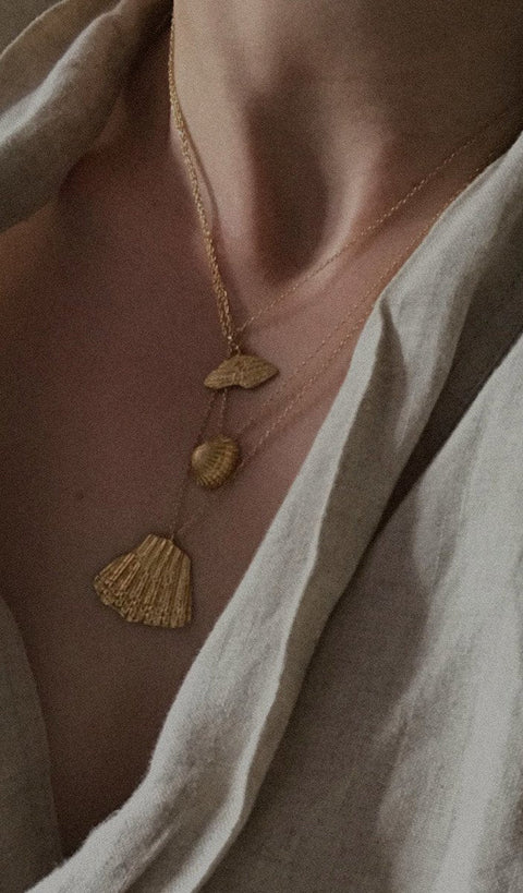 An elegant necklace featuring a large broken shell pendant measuring 25 x 25 mm, suspended on a 50 cm delicate chain. Combining organic texture with minimalist form, it is an ideal accent for summer looks. Beautiful worn alone or layered with the MARE I pendant. Discover refined marine elegance by UMIAR jewelry.