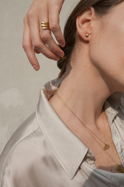 A delicate pendant inspired by the form of a broken shell, measuring 10 x 20 mm and suspended on a 40 cm chain. Combining organic texture with minimalist abstraction, this necklace captures timeless marine elegance. Ideal for summer looks and layering with the MARE II pendant. Discover refined seaside design by UMIAR jewelry.
