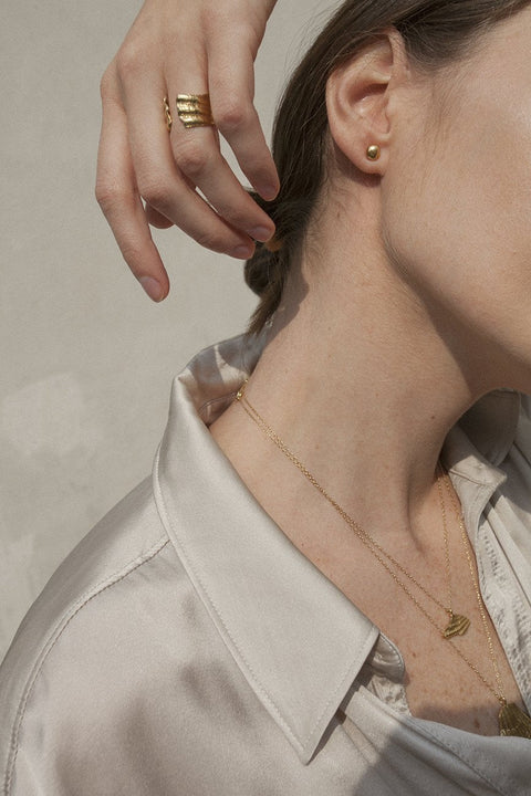 An elegant necklace featuring a large broken shell pendant measuring 25 x 25 mm, suspended on a 50 cm delicate chain. Combining organic texture with minimalist form, it is an ideal accent for summer looks. Beautiful worn alone or layered with the MARE I pendant. Discover refined marine elegance by UMIAR jewelry.